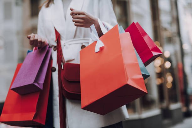 Close up of lady in white trench coat holding colorful shopping bags